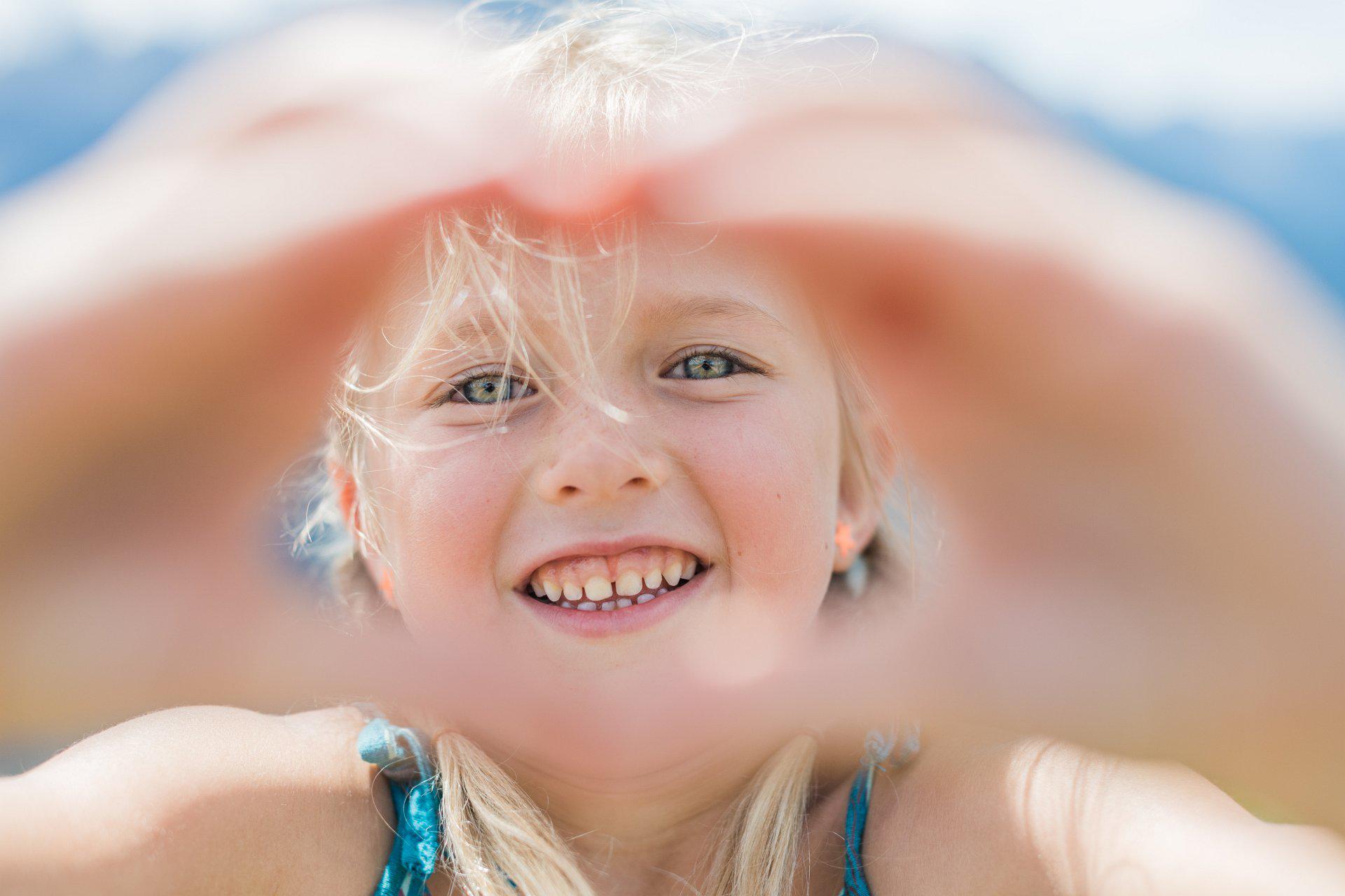 Ein kleines Mädchen streckt beide Hände zu einem Herz geformt in die Kamera.